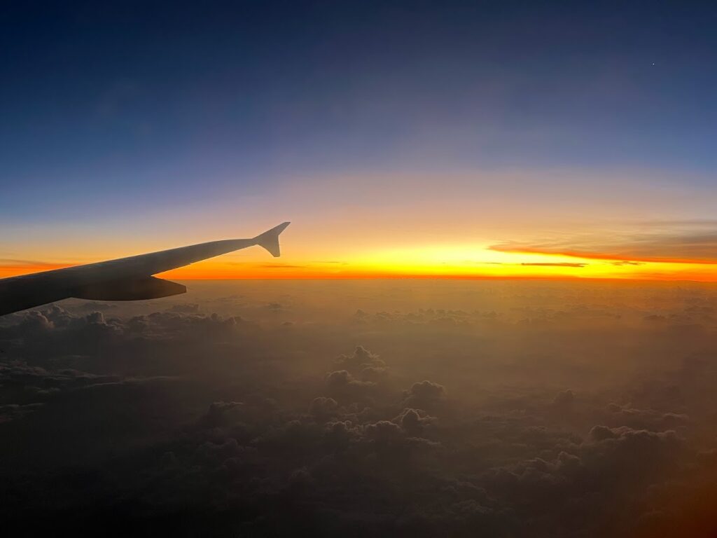 View of the sunrise from an airplane window, with the wing silhouetted against the morning sky, arriving in Cartagena.