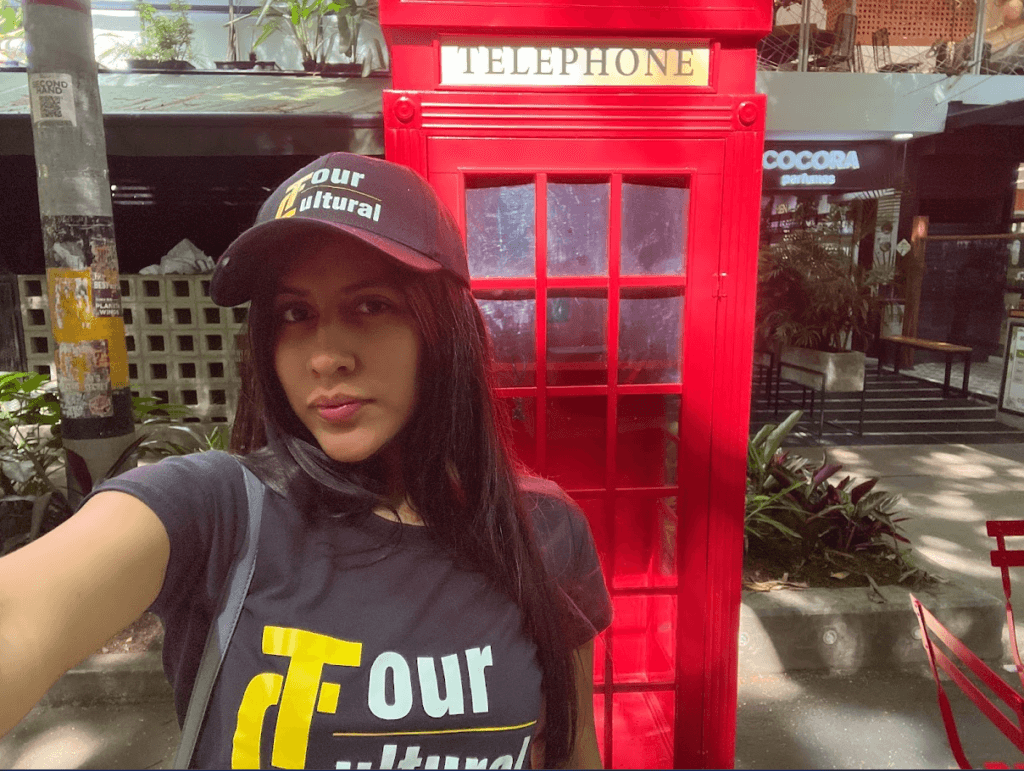 Roxeus in Villa Primavera, Provenza, Medellín, standing in front of a red telephone booth during the day