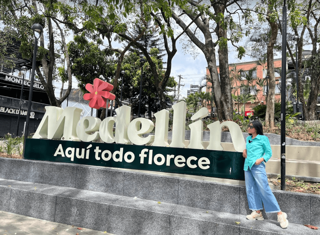 Roxeus standing next to the 'Medellín Aquí todo florece' sign at Parque Lleras in Medellín, Colombia