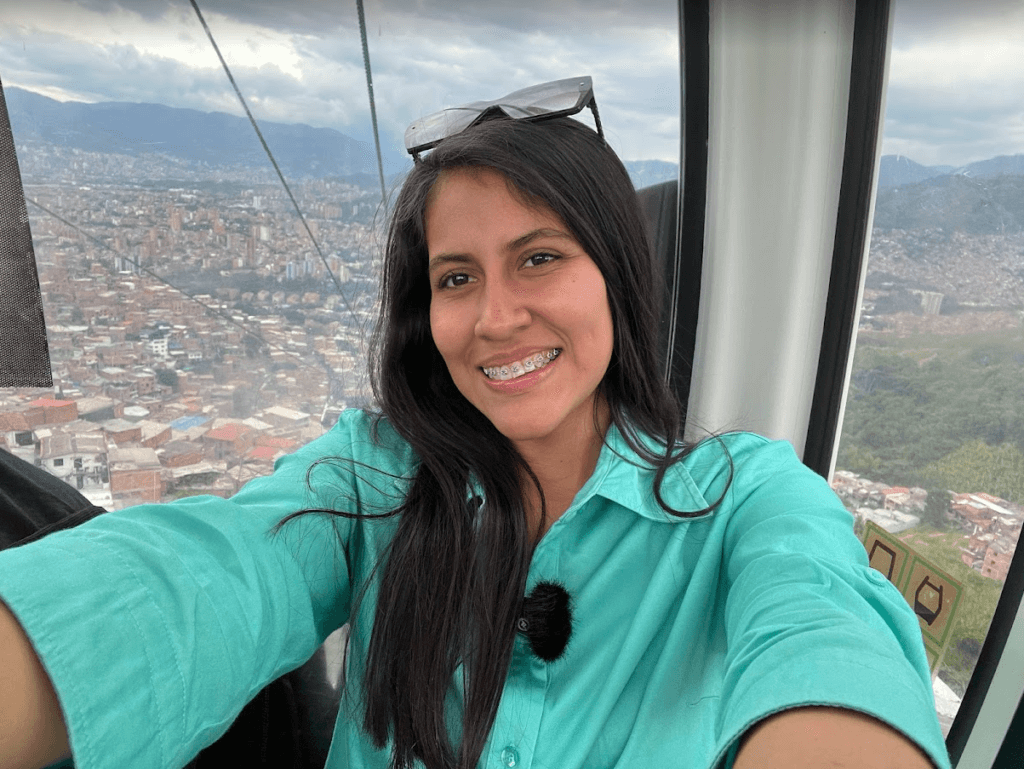 Roxeus taking a selfie on the MetroCable in Medellín, Colombia, with a panoramic view of the city in the background